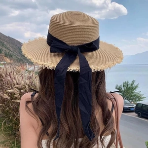 Detail of khaki straw sun hat featuring a black ribbon bow and fringed edges against nature