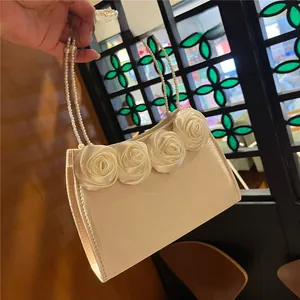 Detail of a creamy satin evening bag with silk roses and faux pearl top handle