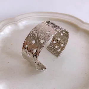 Brazalete ancho plateado con textura martillada, detalles calados y diseño moderno