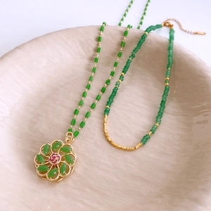 Detail of 18k gold plated glass beaded flower necklaces layered in a white matte tray