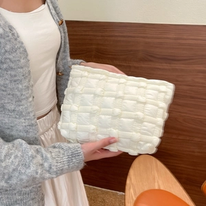 Quilted white cloud makeup bag with puffy grid texture held by a person in a minimalist setting