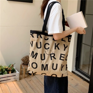 Detail der khakifarbenen Canvas-Tasche mit Lucky-Buchstabenprint und schwarzem Smiley