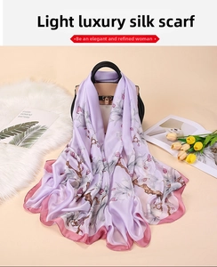 Detail of elegant lavender silk scarf with white magnolia prints draped over a black leather bag