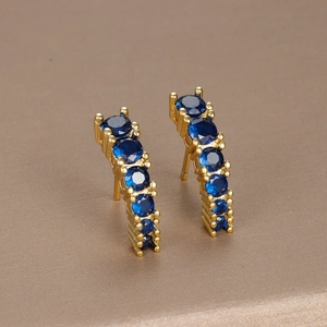 Elegant gold curved earrings with blue round gemstones on a textured background