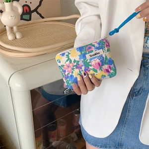 Close-up of floral canvas mini pouch with blue woven handle held by a hand