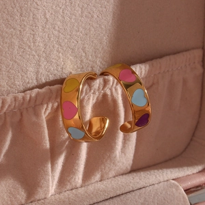 Macro shot of gold-plated hoop earrings with colorful enamel hearts on velvet box