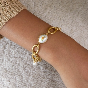 Gros plan du bracelet chaîne en or avec breloque florale et perle sur le poignet