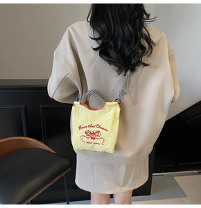 Detail of yellow nylon bag featuring butterfly embroidery and checkerboard handle
