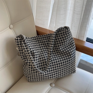 Detailed texture of a black and white houndstooth knit tote bag on a stylish armchair