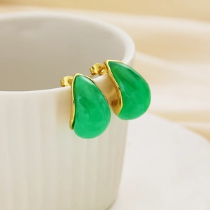 Close-up of teardrop resin earrings in green and gold finish hanging on a ceramic cup