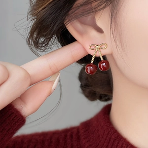 Close-up of cherry drop earrings with golden bows and deep red resin on a model