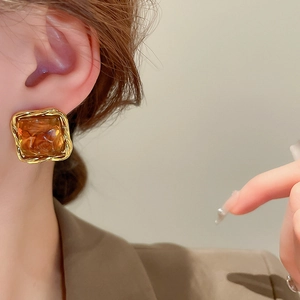 Close-up of golden irregular resin stud earring worn by model in French retro style