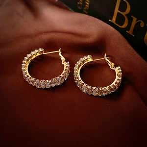 Détail de boucles d'oreilles créoles dorées en C avec zircon sur fond de soie marron