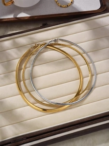 Detailed view of 18K gold and silver snake bone chains on a beige jewelry cushion