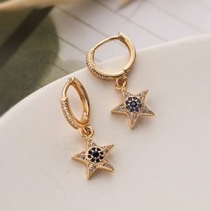 Gold star drop earrings with blue and white zircon stones on a white ceramic base