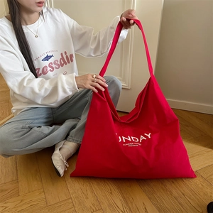 Close-up of red canvas tote bag with white Sunday letter print in a casual home setting