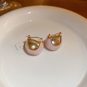 Detail of pink enamel bean earrings in gold plating on a white ceramic plate
