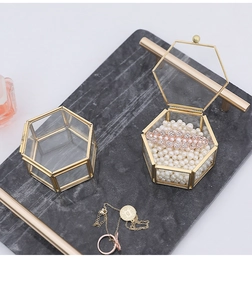Detail view of hexagonal glass jewelry box with gold metal frame on marble tray