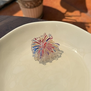 Acrylic flower hair claw with colorful fireworks pattern on a white ceramic tray