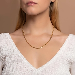 Detail shot of a delicate 18K gold Figaro chain necklace worn by a fashion model