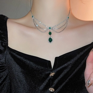 Detailed view of layered silver necklace featuring emerald green zircon pendants on a model