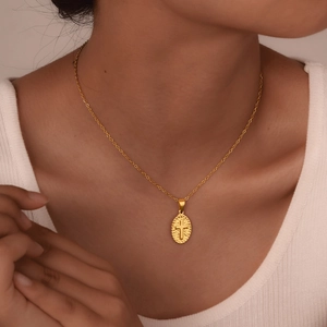 Detail of vintage golden cross oval pendant with hammered texture on female model neck