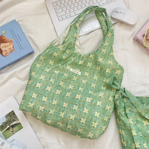 Detailed flat lay of green floral tote bag with white logo label on rustic fabric background