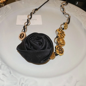 Dettagli della rosa in raso nero e dei ciondoli dorati sulla collana stile vintage