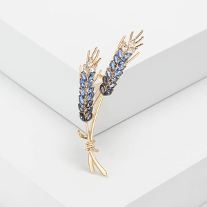 Detailed close-up of a golden wheat ear brooch with blue and white crystals on a white base