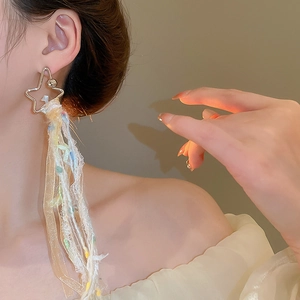 Détail de boucles d'oreilles étoile avec rubans de soie et pompons en dentelle sur modèle