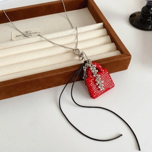 Vue détaillée du collier pendentif sac rouge avec glands dans son écrin brun