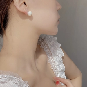 Detail view of large white round pearl earring worn on model for style reference