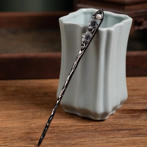 Detail of dark floral hair pin with white pearls on a light green ceramic vase