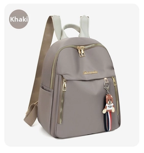 Detail of khaki oxford fabric backpack with golden zippers and a bear pendant accessory