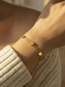 Double-layered gold stainless steel heart chain bracelet worn on a model's wrist