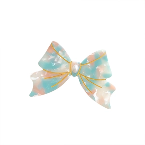 Elegant marble pattern bow hair ring with gold trim and pearl center on white backdrop