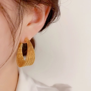 Detailed close-up showing gold geometric hoop earrings with textured layered metal lines