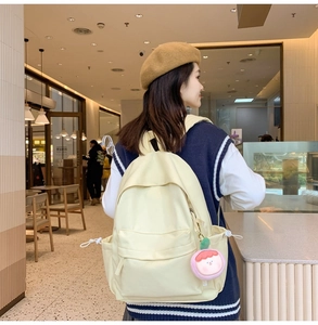 Detailed back view of a beige casual backpack with a cute pink plush charm accessory