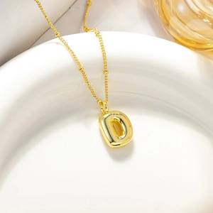 Macro del ciondolo a lettera D a bolla placcato oro 18K su superficie in ceramica bianca