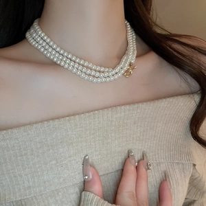 Three-layer faux pearl necklace with gold OT buckle on model wearing ribbed knitwear