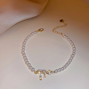 Detail view of pearl bracelet with gold bow pendant and sparkling zircon accents