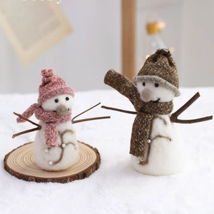 Handmade felt snowman ornaments with knit hats and wooden arms on a rustic wood base