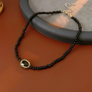 Detail of vintage black beaded choker featuring a gold-edged oval pendant on a tray