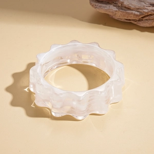 Macro detail of translucent milky white wavy acrylic bangle on a natural wood block