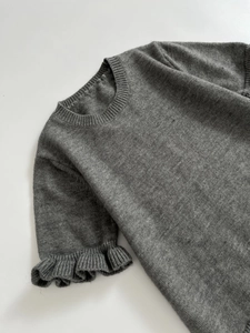 Detail of dark grey knit sweater showing round neck and ruffle edge cuffs texture