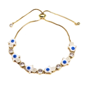 Detail of adjustable golden Hamsa Hand bracelet with white enamel and blue evil eye charms