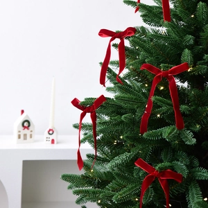 Classic red velvet Christmas bows with long streamers hanging on a lit Xmas tree
