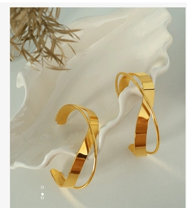 Macro detail of gold intertwined irregular open bangles on minimalist ceramic plate