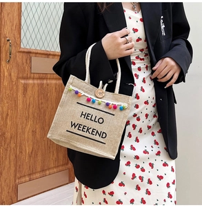 Detail of linen tote bag with colorful pom-poms and HELLO WEEKEND text print