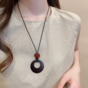 Detail shot of a dark brown resin ring pendant necklace with amber bead on a model